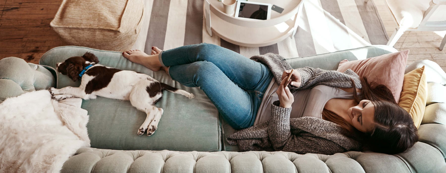 overhead shot of woman looking at her phone as she and her dog lay out on couch